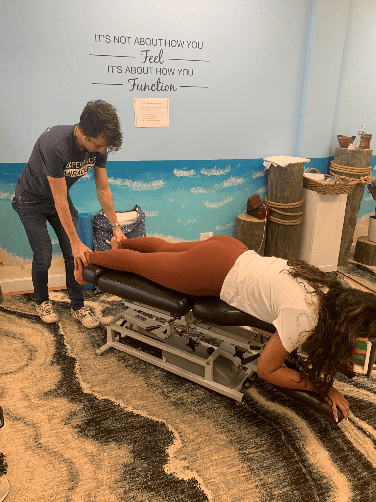 Practitioner checking a woman's legs on a chiropractic table beneath a wall quote