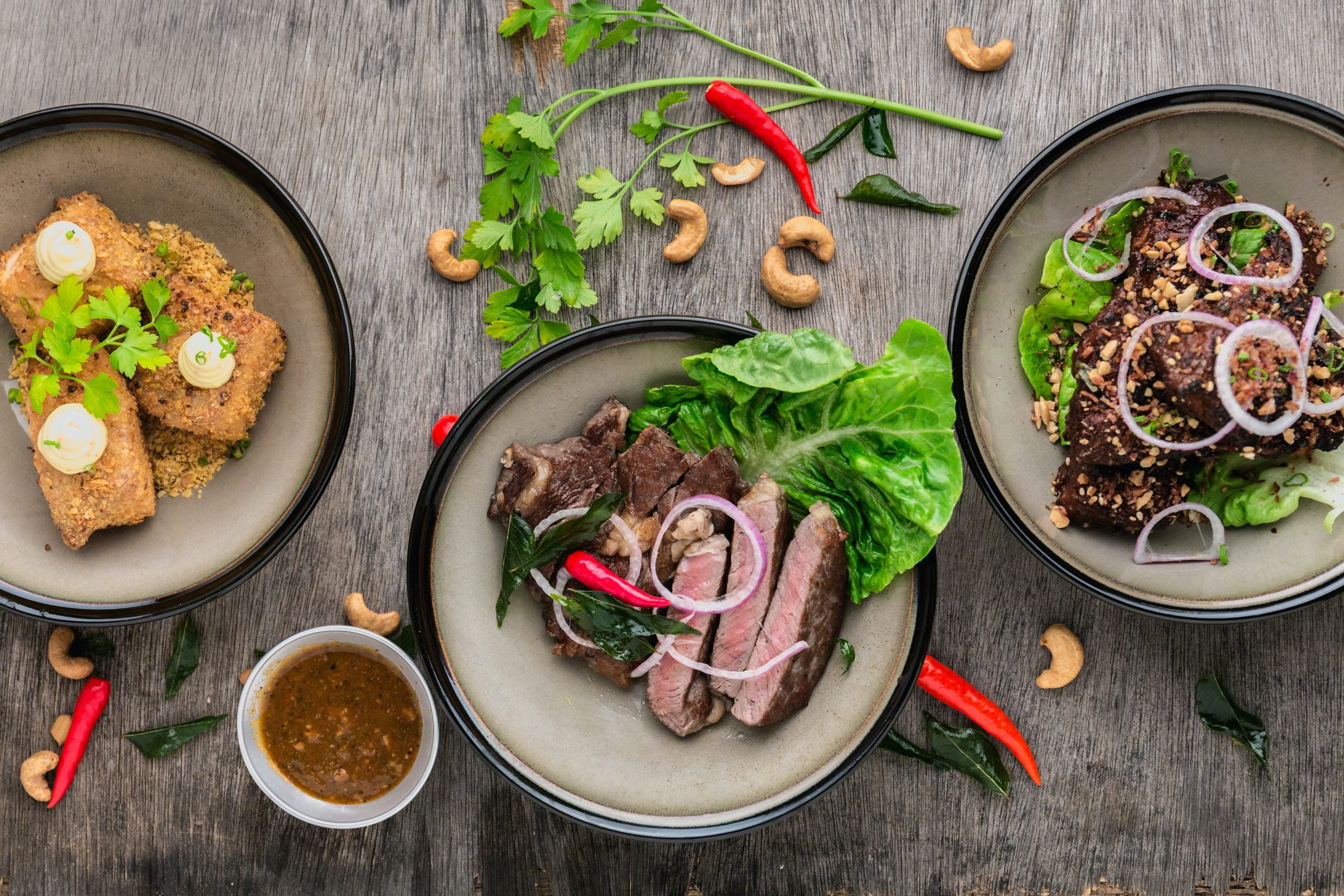 Overhead view of three plated dishes with lettuce, onions, chilies, and cashews