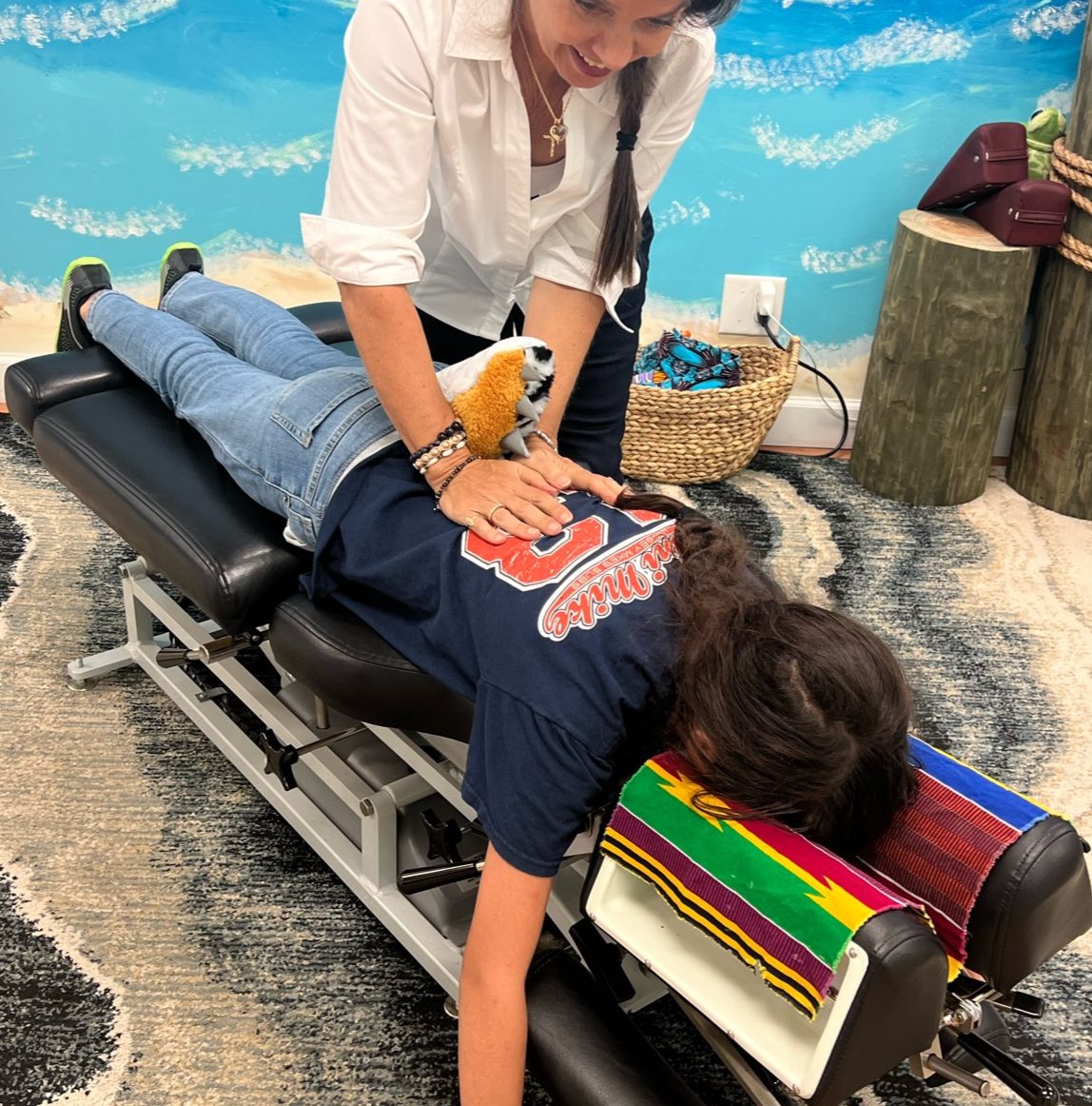 Dr. Karolyn performing a prone adjustment on a patient with a stuffed animal on their back