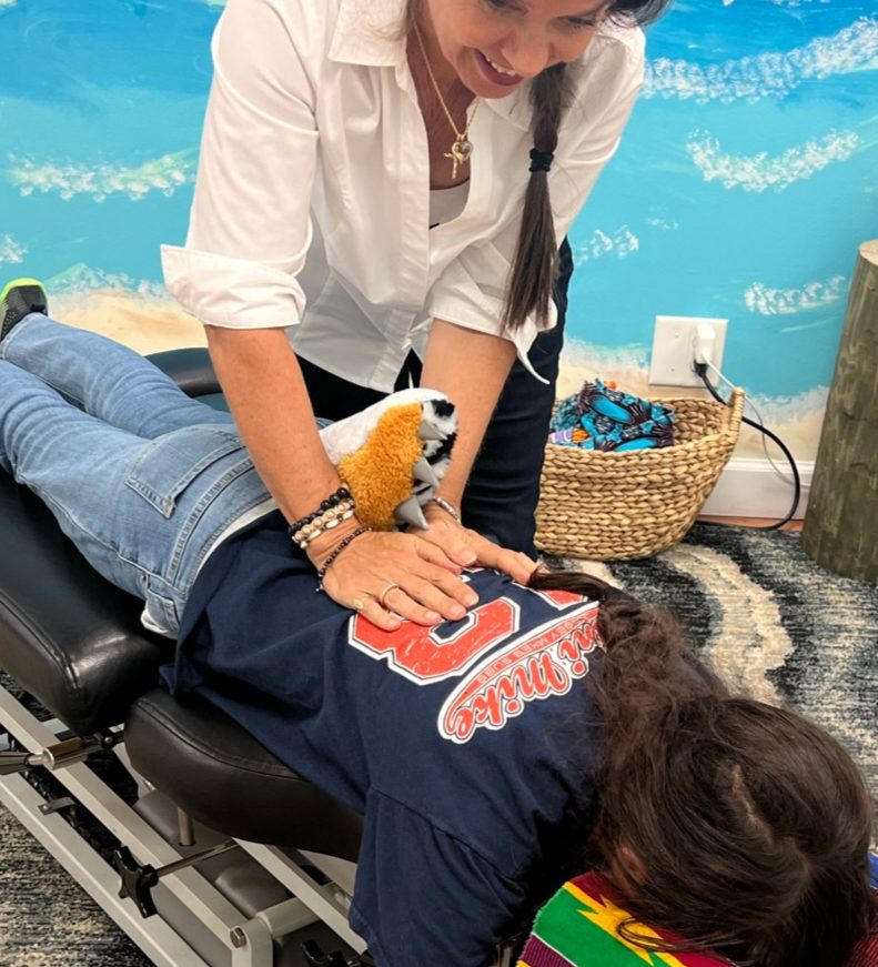 Dr. Karolyn performing a prone adjustment on a patient with a stuffed animal on their back