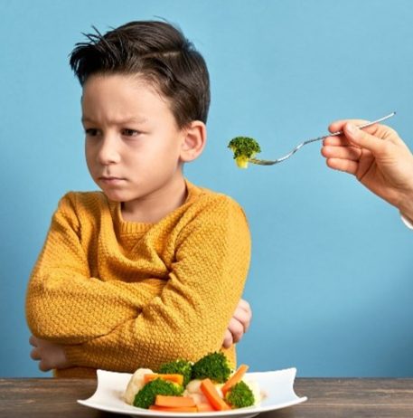 Boy turning away from a fork of broccoli over a plate of vegetables