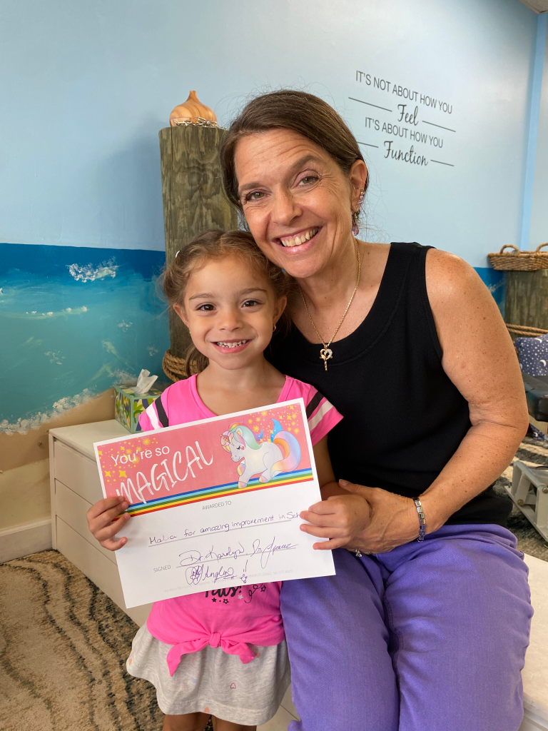 Girl holding a You're So Magical award certificate with Dr. Karolyn
