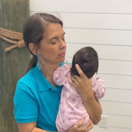 Woman in a turquoise shirt holding a newborn baby in the office