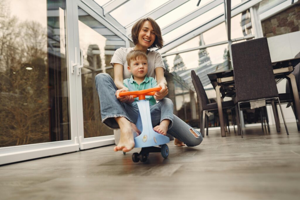 Mother riding a toy scooter indoors with her young son