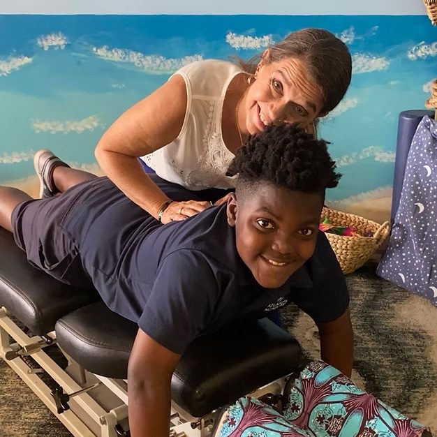 Dr. Karolyn smiling beside a boy on a chiropractic table